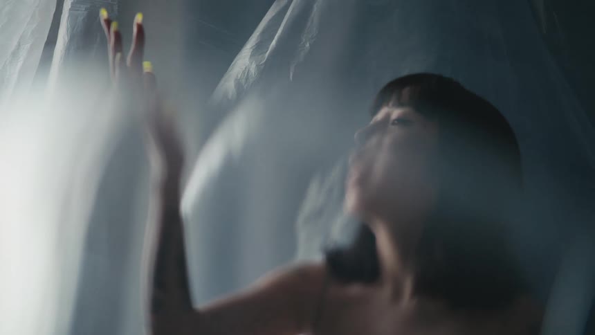 A woman looking at her long fingernails in front of a billowing plastic sheet