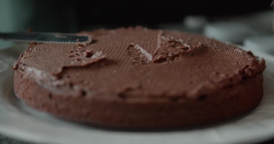 Person rotates plate while spreading chocolate icing on cake with cake spatula
