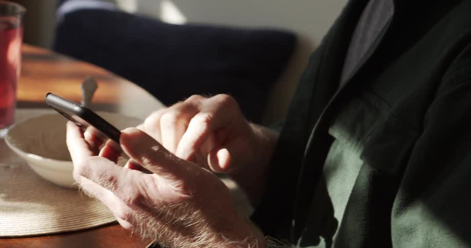 A man sitting at the table with a meal smiles as he uses his cell phone