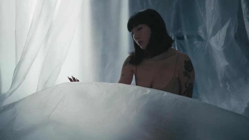 A tattooed woman sits atop a large sheet of flowing sheer fabric