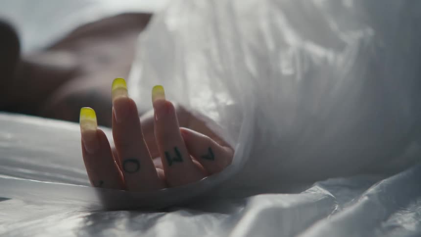 Plastic sheeting is pulled out from around and under a womans hand with yellow tipped finger nails