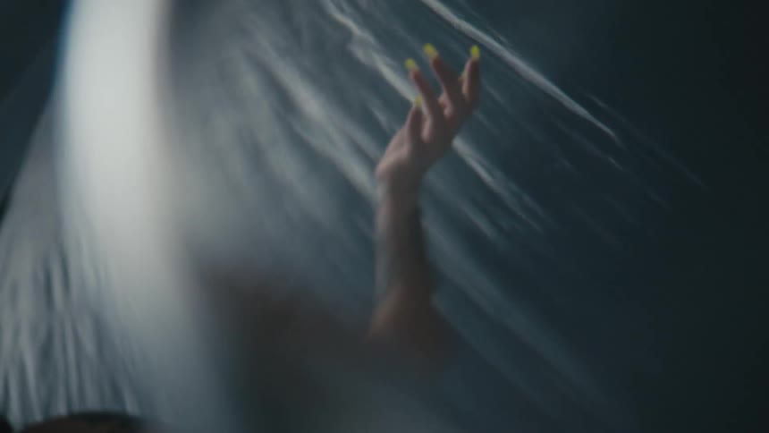 A woman holds her hand upwards in the air while surrounded by a large sheer sheet of fabric