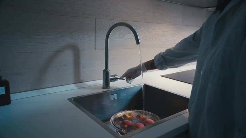 A person adding water to a bowl of apples