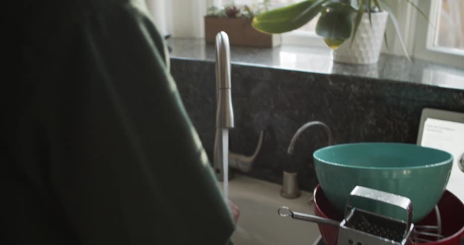 A man stands at his kitchen sink rinsing bowls and mixer blades