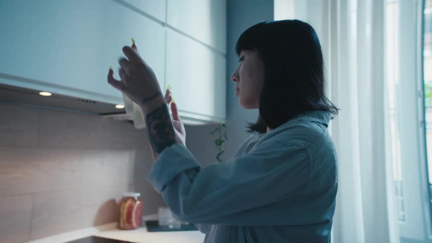 A woman in a kitchen taking off a glove with a wall and window in the background