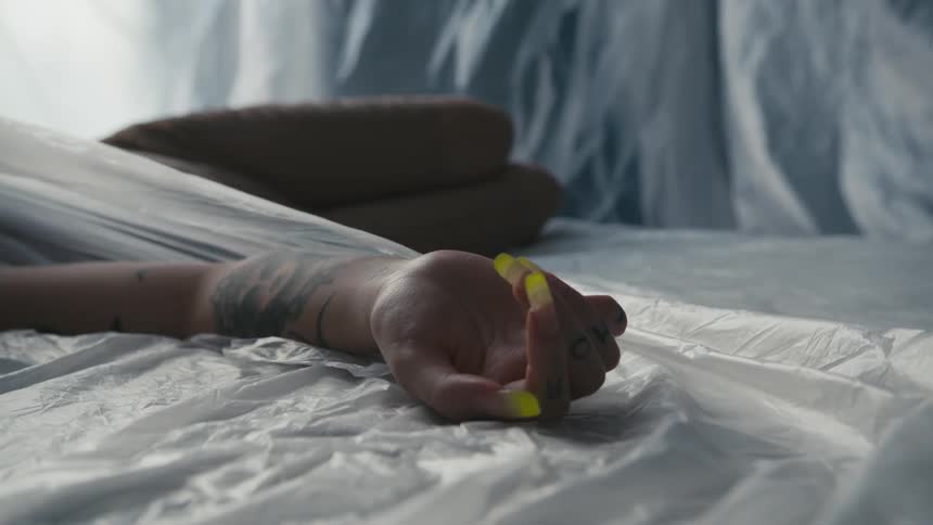 A woman lays on the floor motionlessly while surrounded by fabric