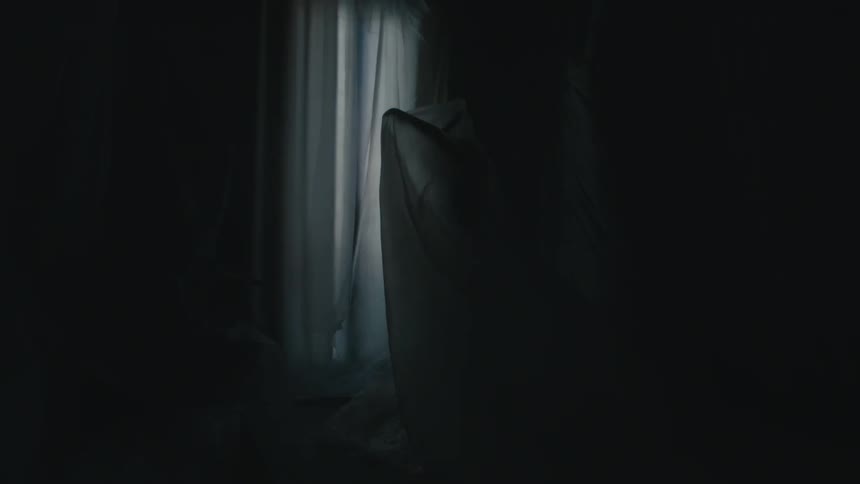 A woman extends her arms while beneath a draped sheer piece of fabric