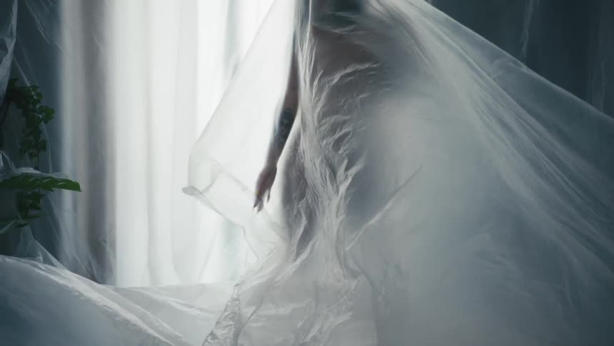 A woman holds her arms outward while covered by a large sheer sheet of fabric
