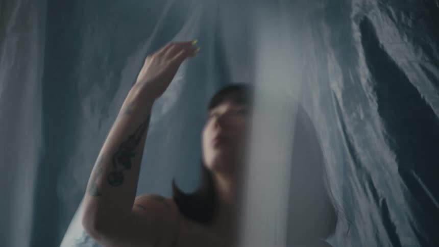 A woman gazes at her outstretched hand while surrounded by plastic sheets