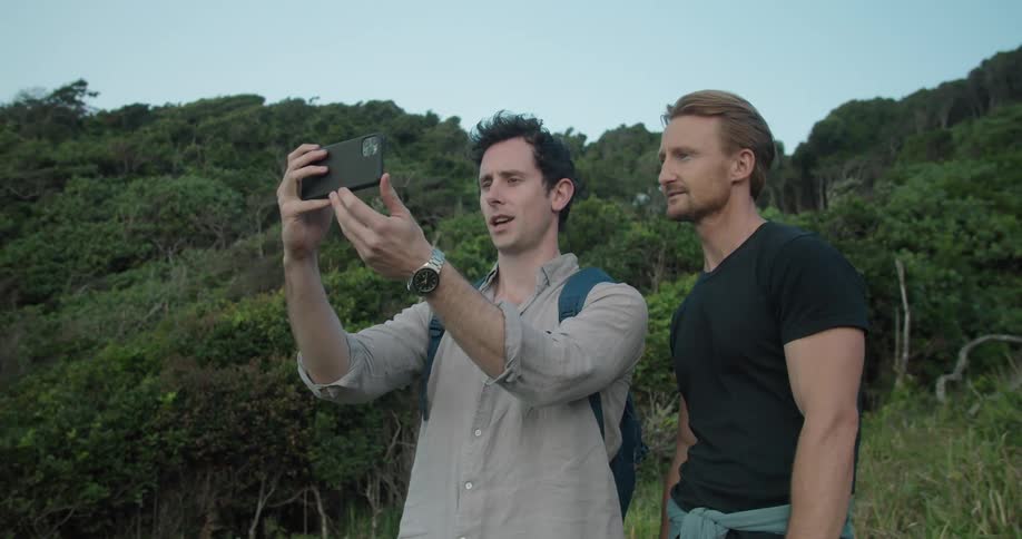 Two men stand outdoors while one holds up his phone to take a photo