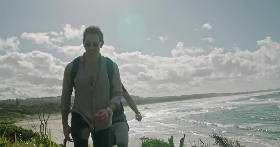 A pair of men chat while walking up a hill behind a beach on a sunny day