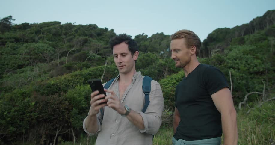 Two men discus picture one is taking with mobile phone standing on hill near forest