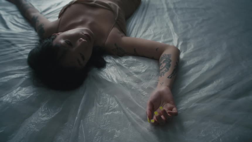 Woman with a brown shirt and tattoos lies on bed
