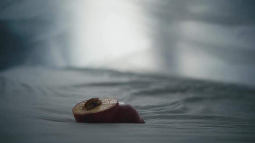 A peach sliced in half resting on a plastic bag in a room with a window in the background