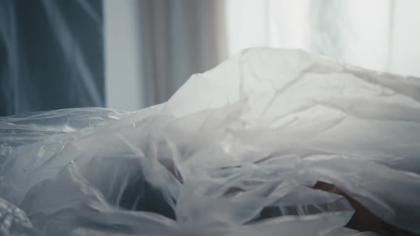 Plastic covering unmoving staring woman lying on back is pulled away