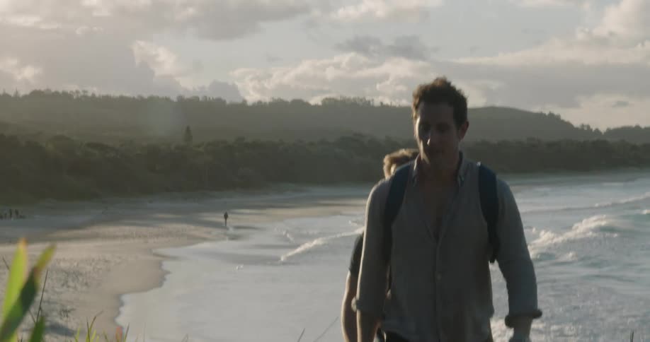 Two men hike up hill near shore as wave crash onto misty shore