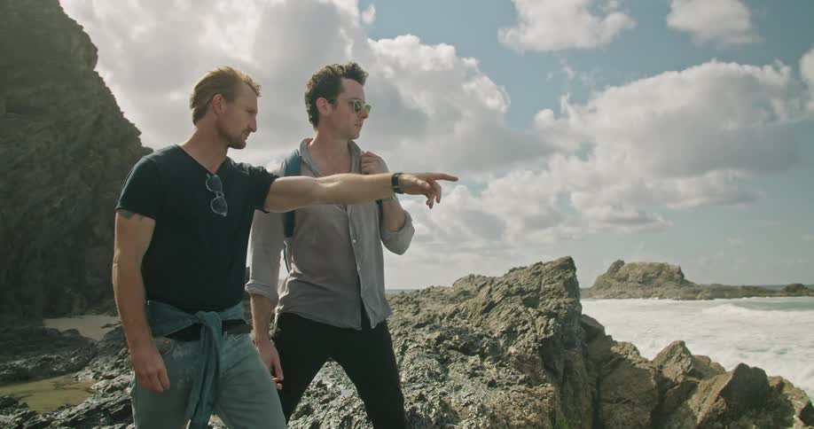 A pair of men speak while approach the edge of a rocky coastline during the day