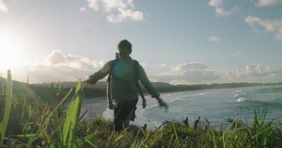 Two men hike through a grassy field away from the ocean