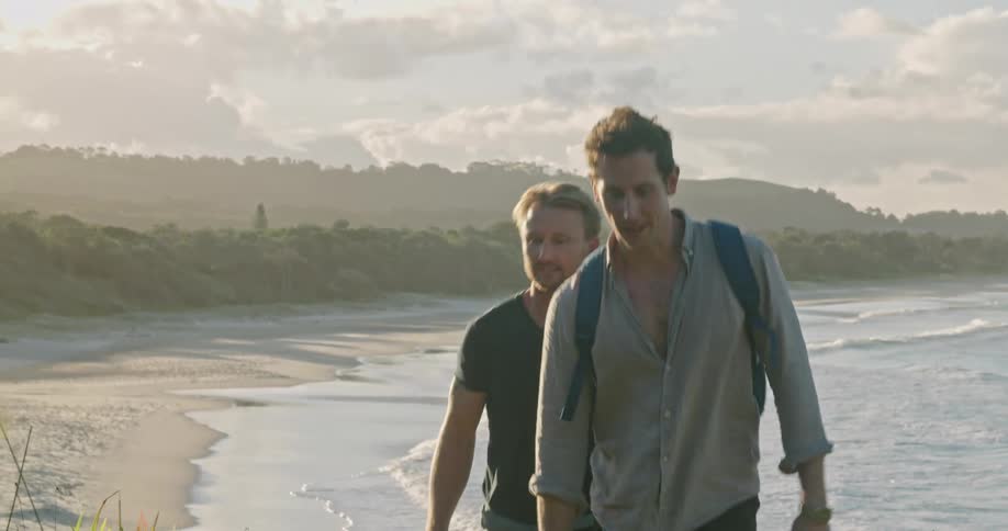 A pair of men walk up a hill overlooking a sandy beach during the day