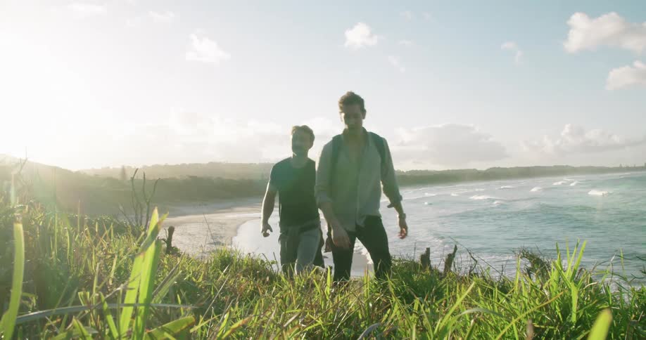 Two men climb up slope away from beach on sunny day as waves roll onto sand