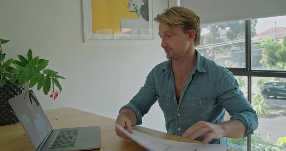 Blonde man with a shirt sits at table and works on laptop in the office