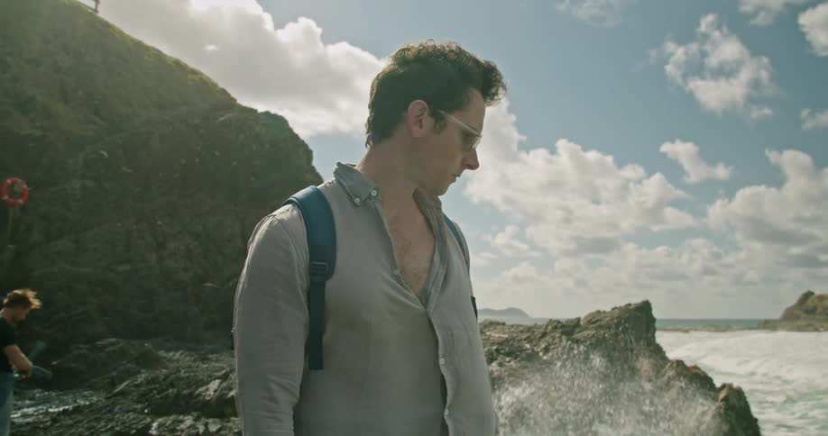 Two men standing on a rocky shore with the sky and clouds in the background
