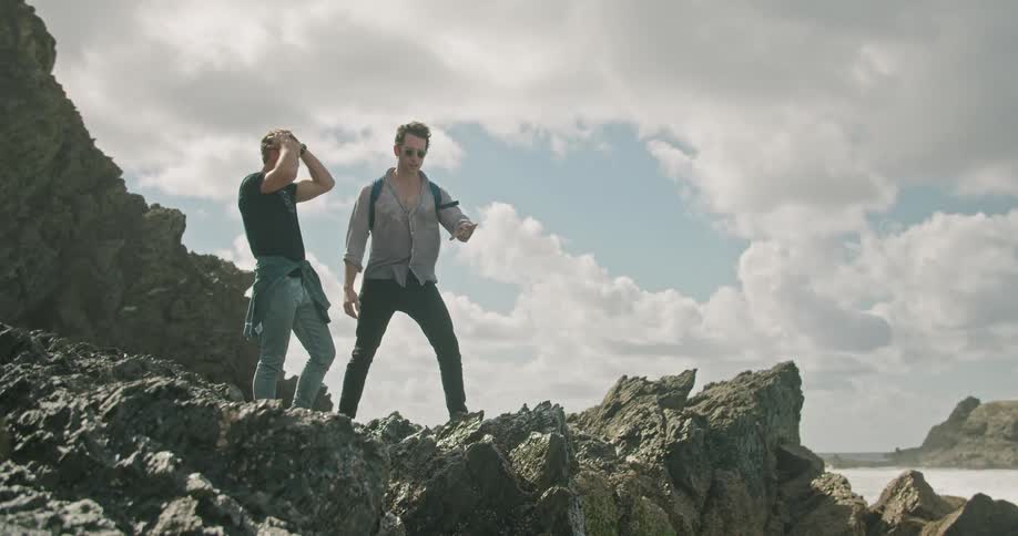 Two men stand on the rocks of the rough shore