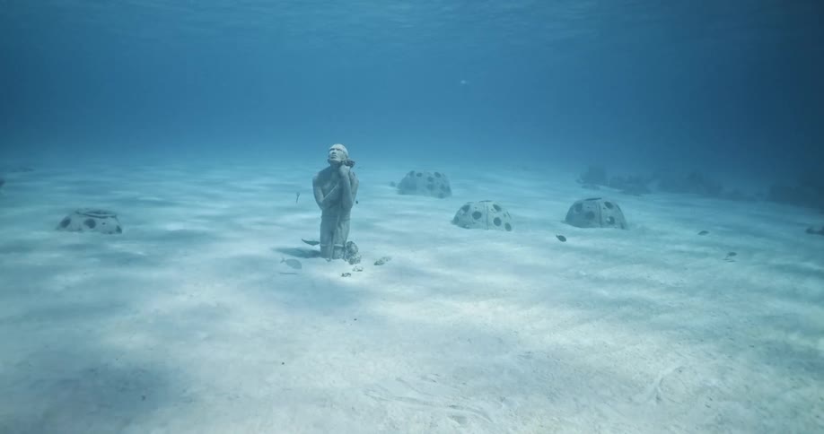 An underwater sculpture of atlas looks up at the surface in a blue sea
