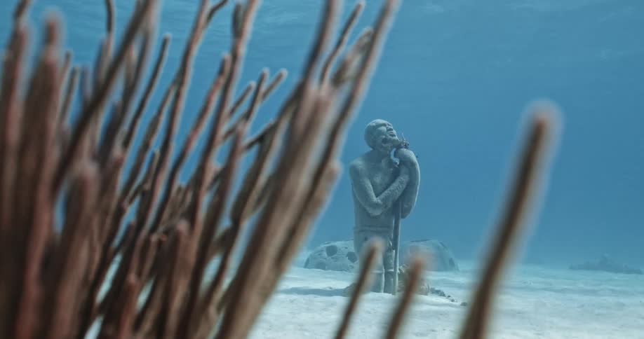 A kneeling statue and seaweed on an ocean floor