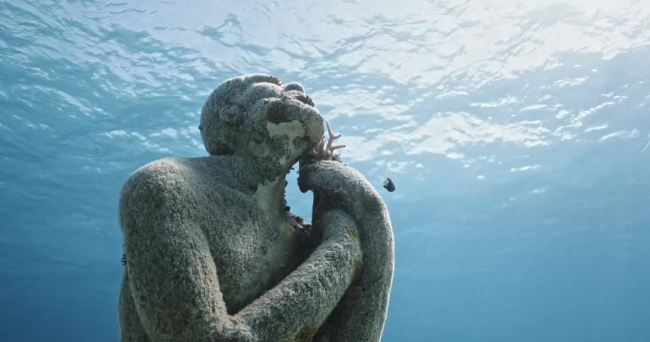 An underwater view of a fish swimming around a statue under water