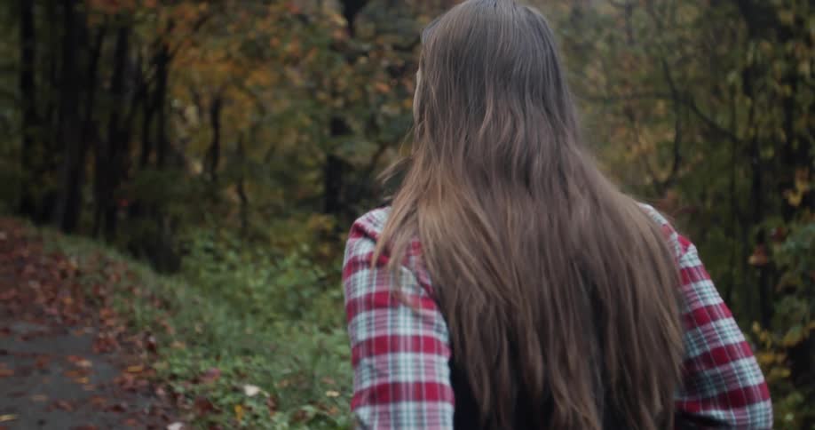 A woman in a flannel shirt walks down a road through a forest