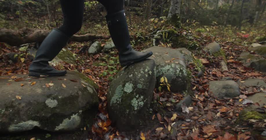 A person in boots walking on boulders in a forest