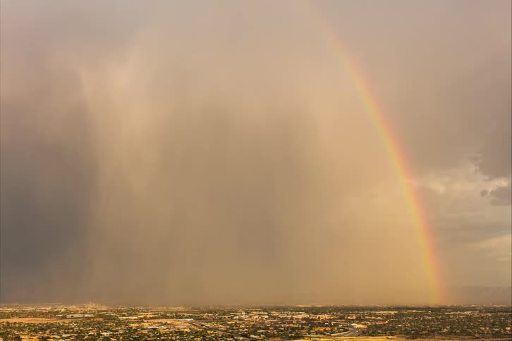 A landscape view with cars driving on streets and a large rainbow in the cloudy sky