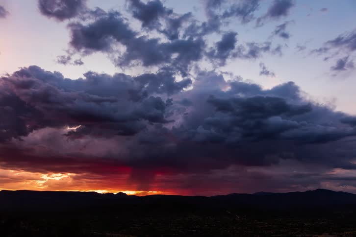 Dark storm clouds move over small town and mountains in red sky