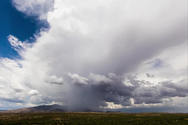 Blue skies hide behind dark clouds as a storm sets in over a field