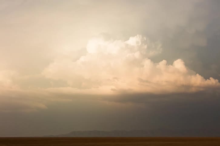 Storm clouds obscure mountains on horizon and fill sky over plains as they start to rotate