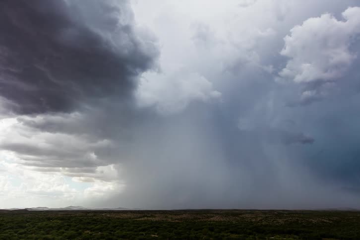 Storm clouds pass overhead in the sky and release torrents of rain onto the ground below