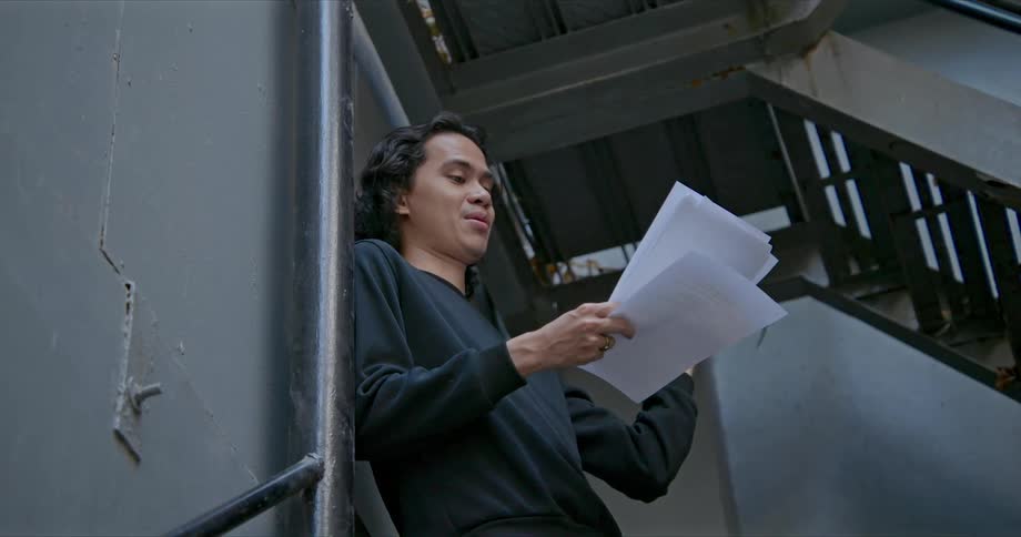 A teenager reads from a stack of papers while standing in a stairwell