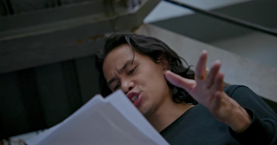 A man holds up his hand as he rehearses the lines that are written on his pages
