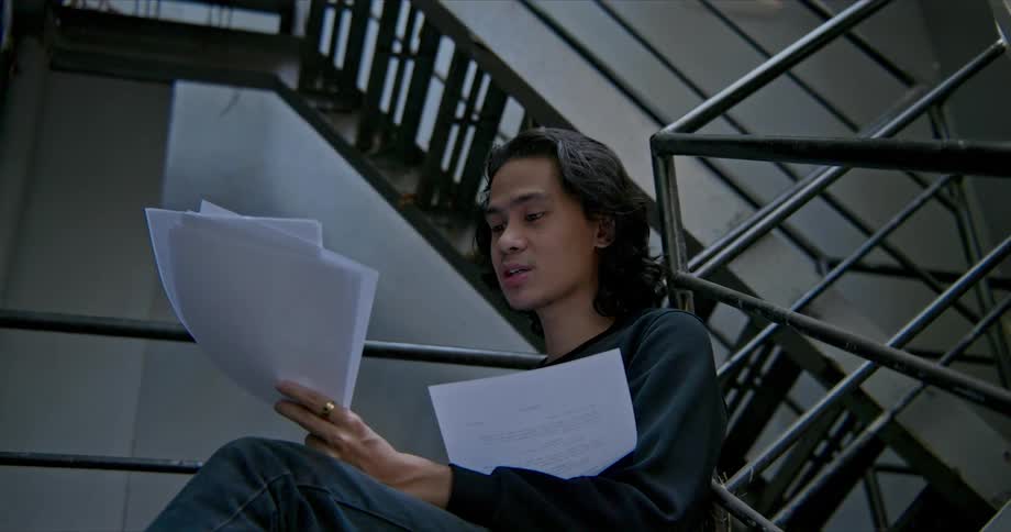 A man in a room with papers sitting on a staircase with a wall in the background