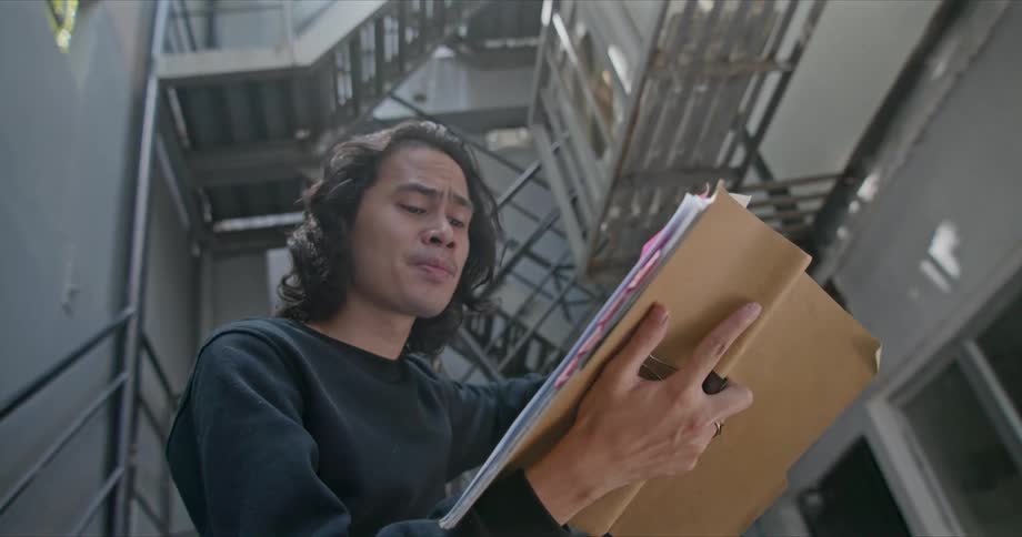 An expressive man rehearses the lines that are written on his papers in a stairwell