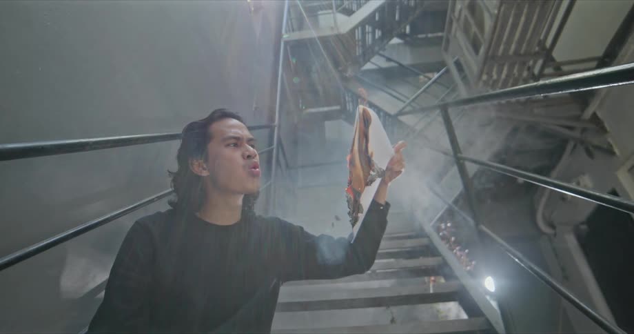 A teenager jeers as he holds a burning folder full of papers in a stairwell