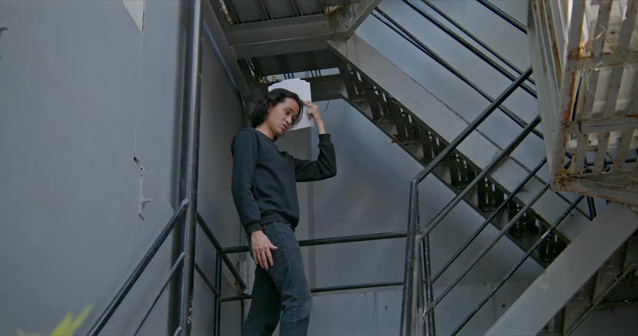 A young man stands in a stairwell and sings