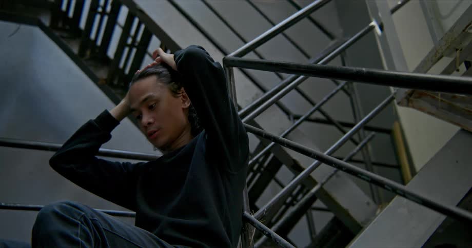 A teenager stands in a building stairwell and reads from a manilla folder of papers