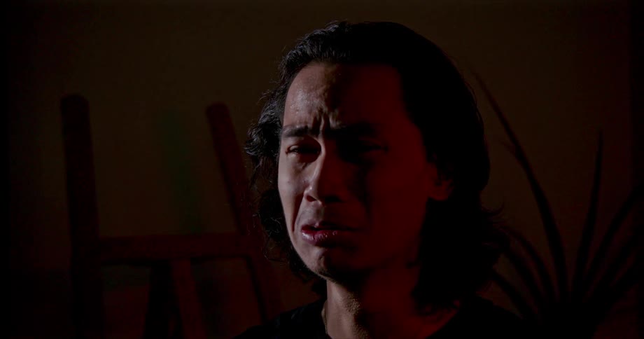A man sits alone in a dark room crying and shaking his head