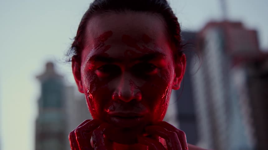 A man smears bright red paint or blood on his face and smiles