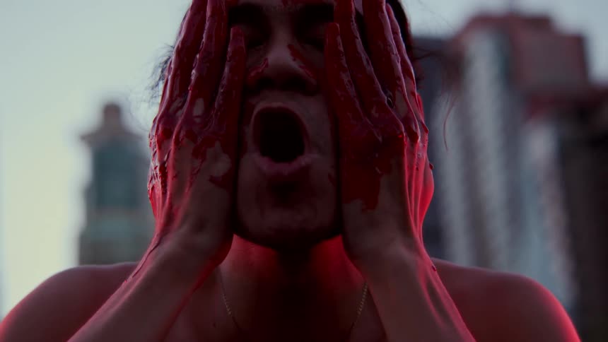 Blood drips from a mans hands and he rubs the blood all over his face