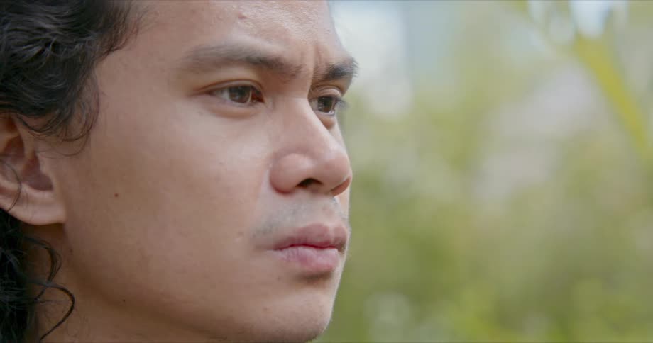 A young man with an angry look on his face is contemplating outdoors