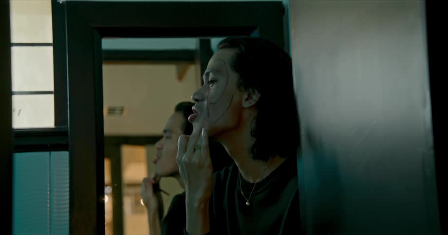 Man dabs his face while standing facing mirror near window