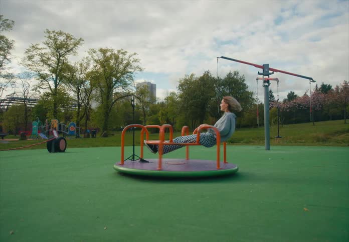A young female reclines on a spinning merry go round while posing for her smart phone camera